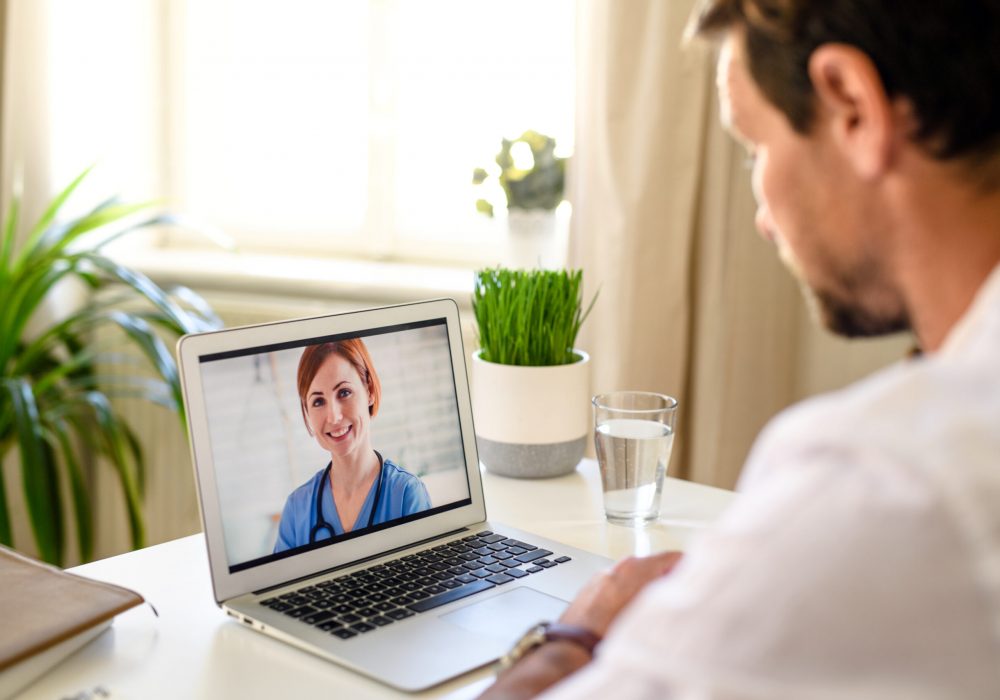 Mature man having video call with doctor on laptop at home, online consultation concept.